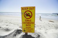 A sign warns of sewage contaminated ocean waters on a beach Wednesday, March 1, 2017, in Coronado, Calif. Coronado and Imperial Beach waters remain closed to swimmers and surfers Wednesday after more than 140 million gallons of raw sewage spilled into the Tijuana River in Mexico and flowed north of the border for weeks in February, according to a report. (AP Photo/Gregory Bull)