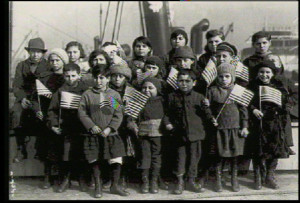 Immigrant children wave flags on Ellis Island, in contrast with many modern day immigrants.